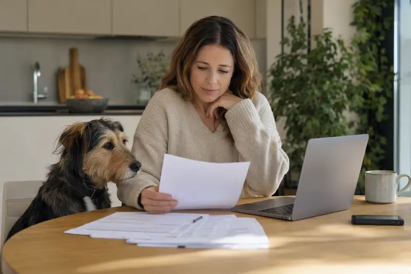 Ein Barak Hund sitzt friedlich neben seinem Besitzer, während sie am Küchentisch Versicherungsunterlagen und einen Laptop mit Vergleichsdiensten durchsehen.