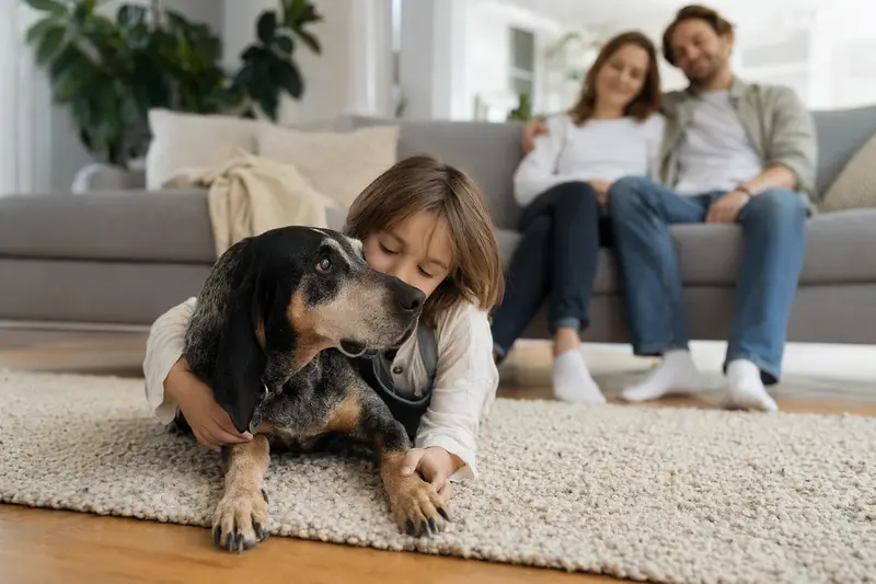 Ein freundlicher Bluetick Coonhound liegt entspannt neben einem Kind im Wohnzimmer in einer sicheren Familienatmosphäre.
