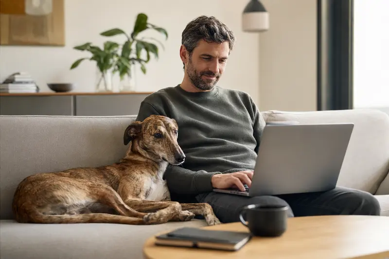 Hundebesitzer mit Charnegui Hund auf dem Sofa, Laptop zeigt einen neutralen Versicherungsvergleich.