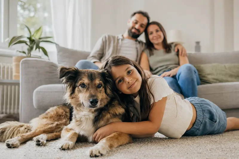 Ein freundlicher Cuvac Slovensky Hund liegt entspannt neben einem Kind in einem hellen Wohnzimmer.