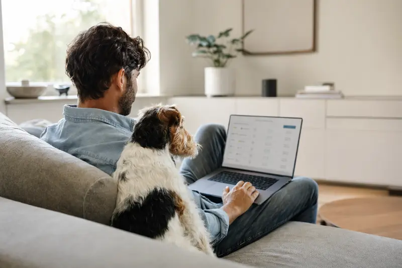 Besitzer arbeitet entspannt am Laptop auf dem Sofa, während ein Drahthaar-Foxterrier neben ihm sitzt, passend zur Entscheidung über Tierversicherungen.