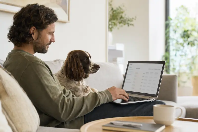Ein Hundebesitzer sitzt mit einem Laptop auf dem Sofa neben seinem English Springer Spaniel und nutzt eine Versicherungsvergleichsoberfläche.