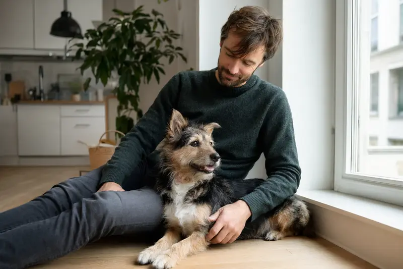 Ein entspannter Kobe-Terrier sitzt neben seinem Besitzer in einer hellen Wohnung.