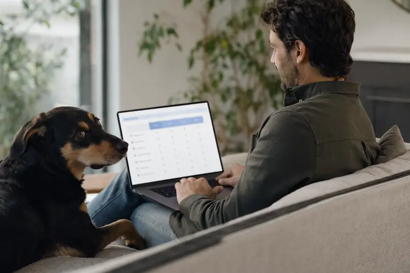 Ein Hund neben seinem Besitzer, der am Laptop sitzt und sich mit Versicherungsvergleichen beschäftigt.