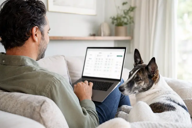 Ein Hundebesitzer mit Laptop auf dem Sofa, neben ihm ein Perro de Ganado Majorero, während er sich über Versicherungsoptionen informiert.