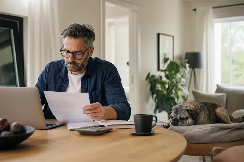 Ein Hundehalter sitzt mit einer Tierarztrechnung am Tisch, während ein entspannter Retro-Mops auf einer Decke liegt und das Thema Tierarztkosten und Hundeversicherung ruhig vermittelt.
