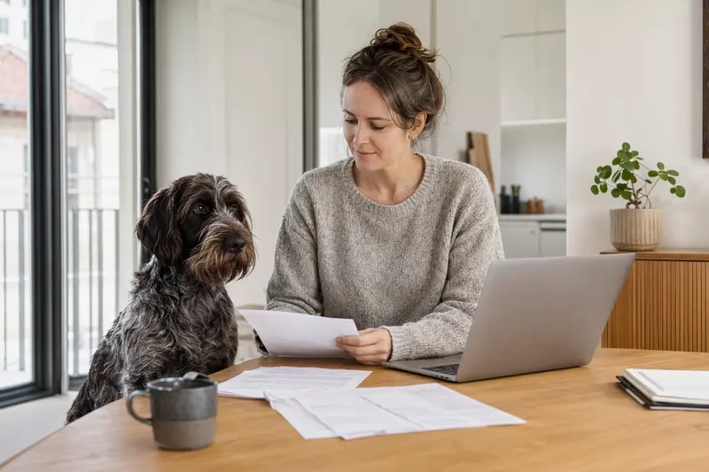 Ein Slowakischer Vorstehhund sitzt ruhig neben seinem Besitzer am Küchentisch mit Versicherungsunterlagen und Laptop zu einer Tierkrankenversicherung.