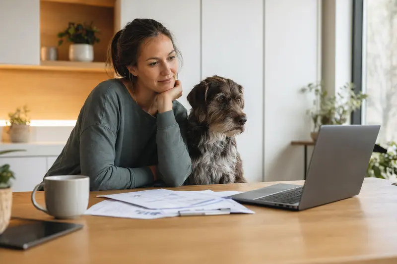 Ein Wachtel Hund sitzt ruhig neben seinem Besitzer am Küchentisch mit Versicherungsunterlagen und Laptop zur Hundekrankenversicherung.